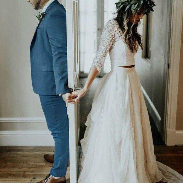 Bride in white lace top and full skirt holding hands with groom in blue suit