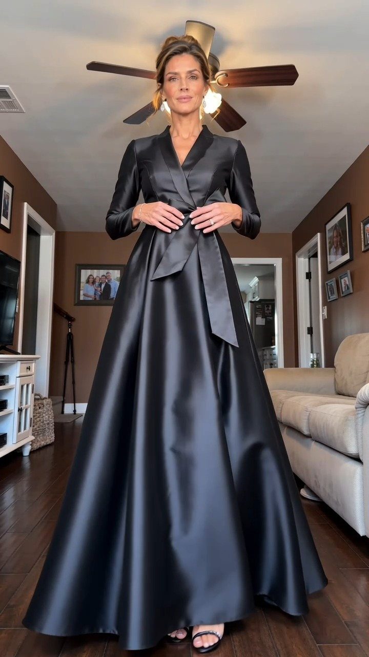 Woman in a long-sleeved black satin wrap dress standing in a living room.