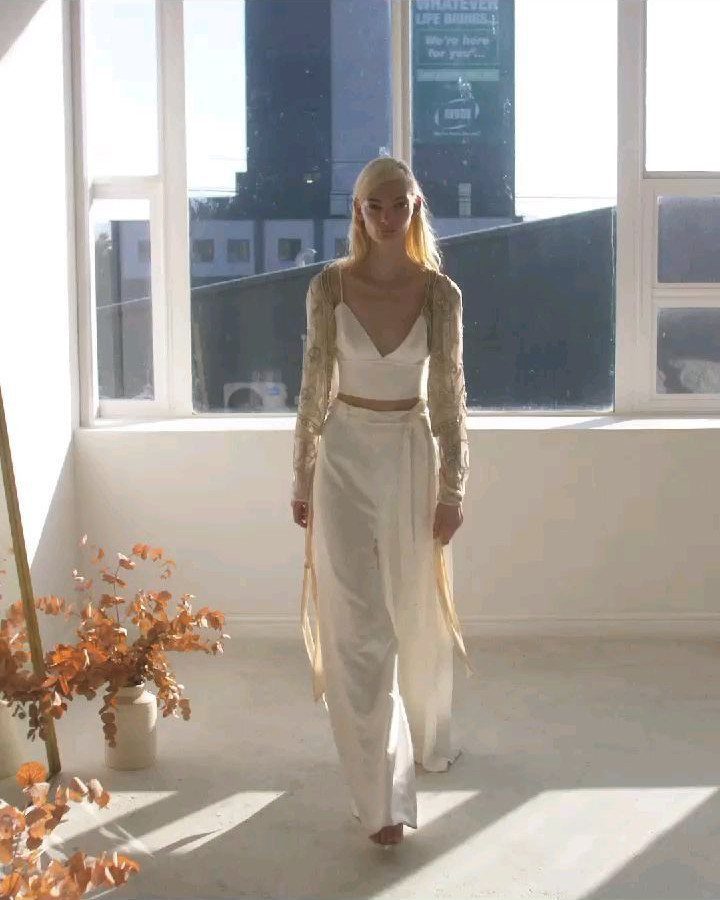 Woman in white wide-leg trousers and cropped top with a beaded cardigan