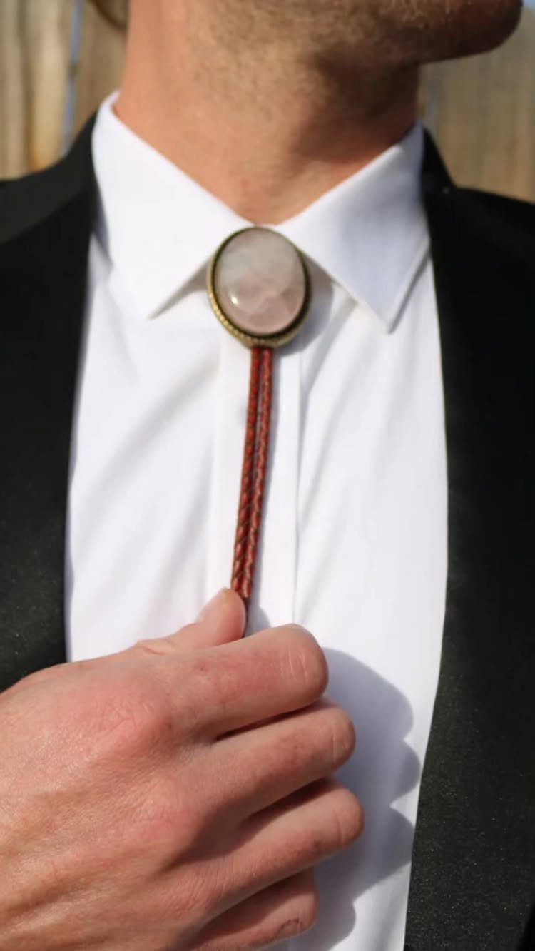 Bolo tie with a pink stone and braided leather cord on a white shirt.