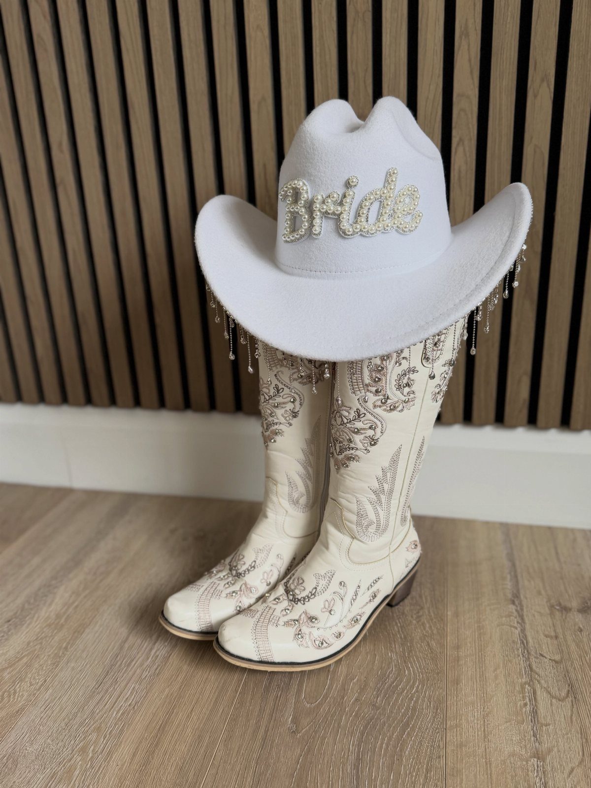 White bridal cowboy hat and embroidered western boots on a wooden floor