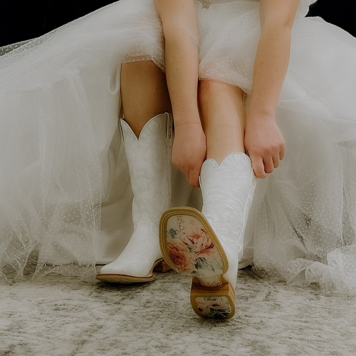 White cowboy boots with floral soles worn under a white tulle wedding dress.