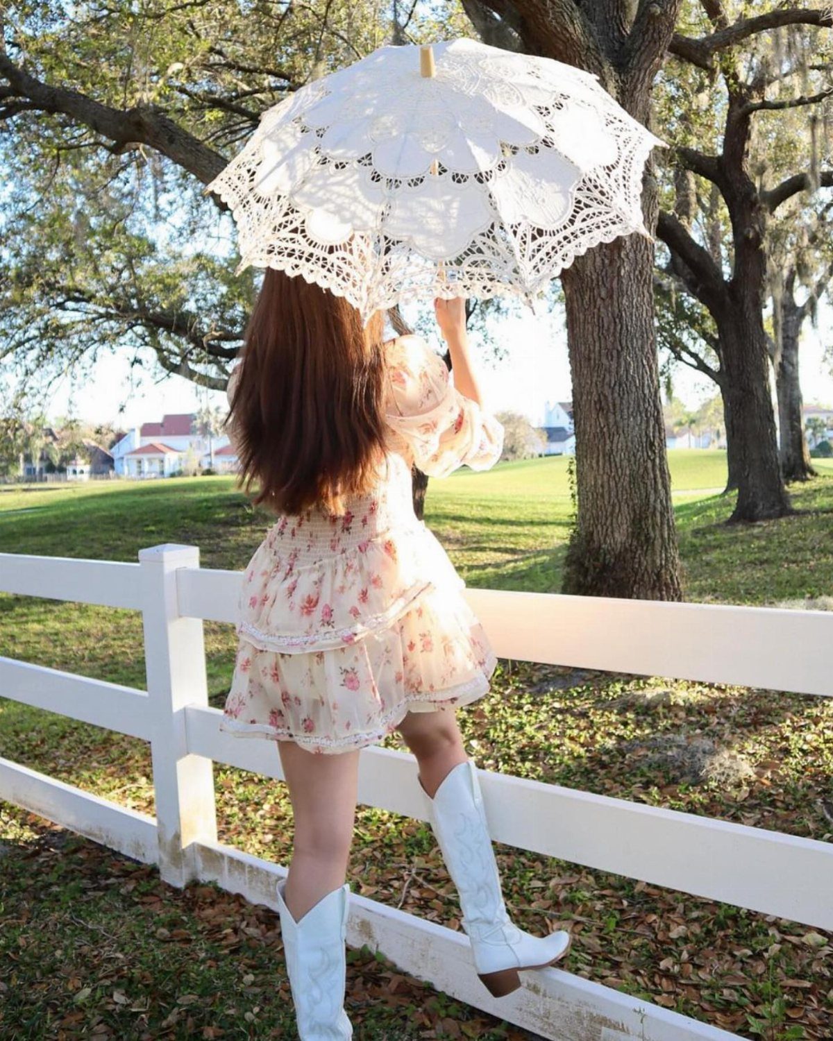 Woman in a short floral dress and white cowboy boots holding a lace parasol.