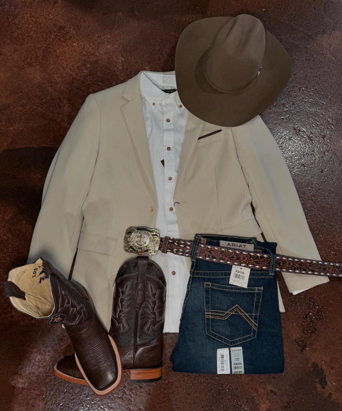 Tan blazer, white shirt, blue jeans, cowboy hat, and boots arranged in a flat lay.
