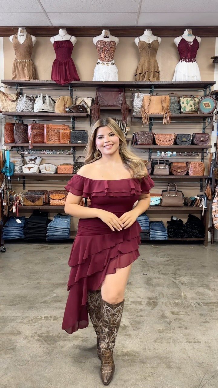 Woman in a maroon ruffle dress and brown cowboy boots in a western store.