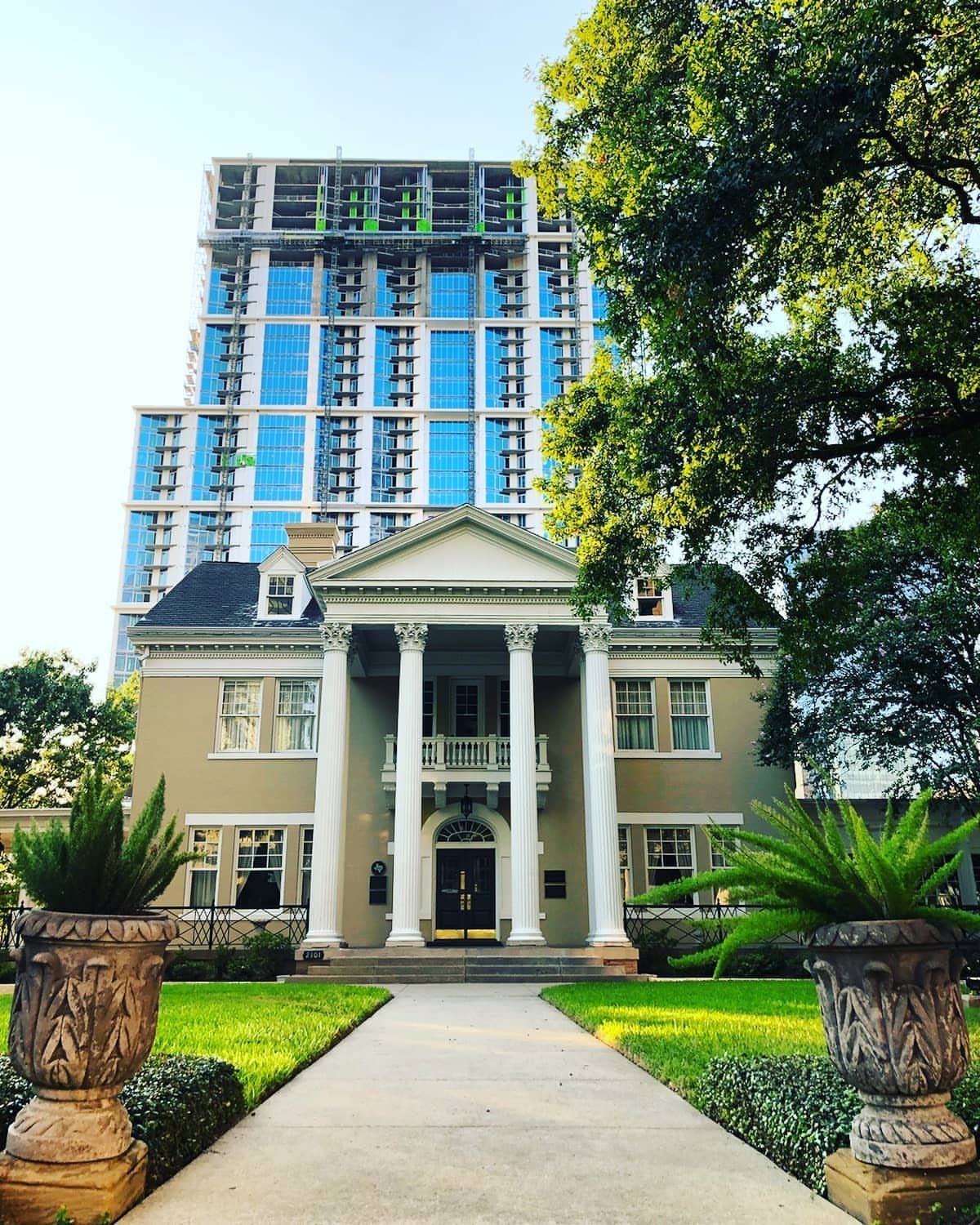 Beige neoclassical mansion with white columns set against a modern blue glass skyscraper.