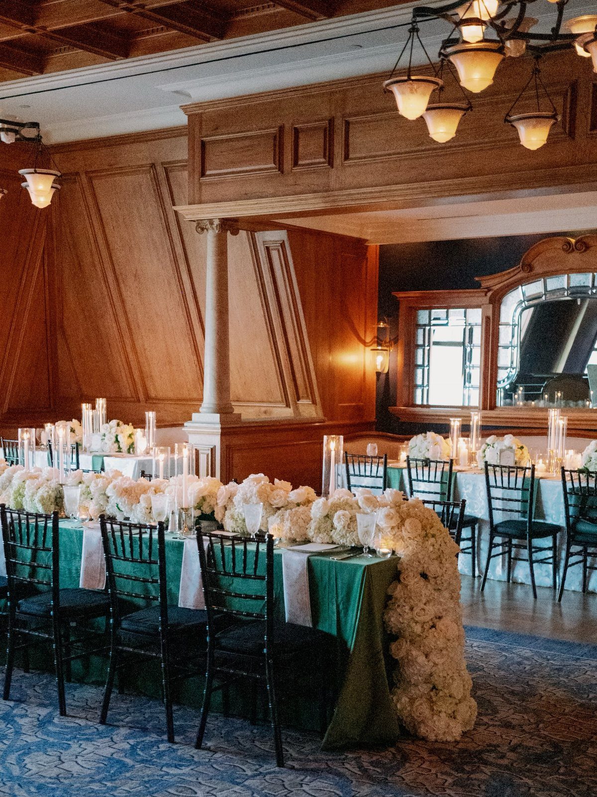 Long dining table with white flowers and green linens in wood-paneled room.