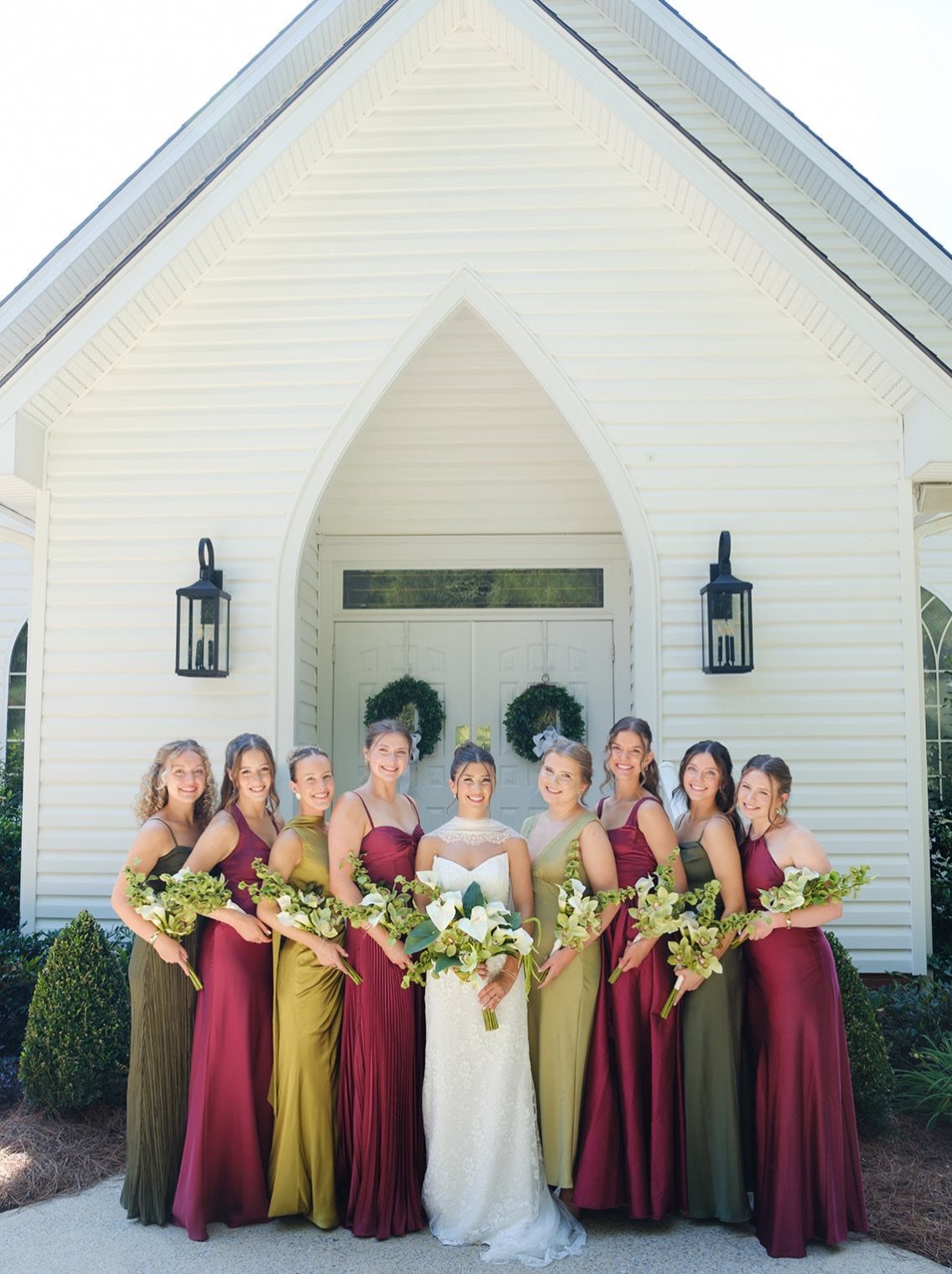 Bride and bridesmaids posing in front of a white wooden chapel with pointed arch.