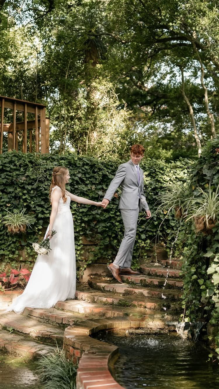 Bride and groom holding hands on brick steps in a romantic garden venue.