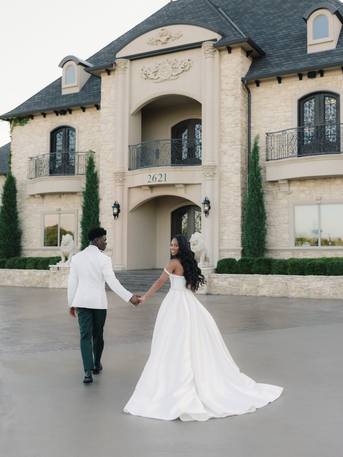 Wedding couple walking toward a luxurious French-inspired stone castle venue with ornate balconies.