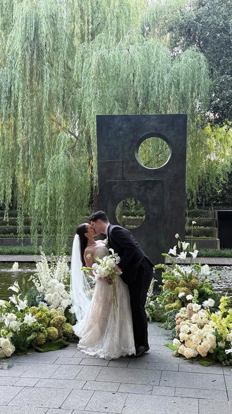 Bride and groom kissing before a modern geometric sculpture and white flowers.