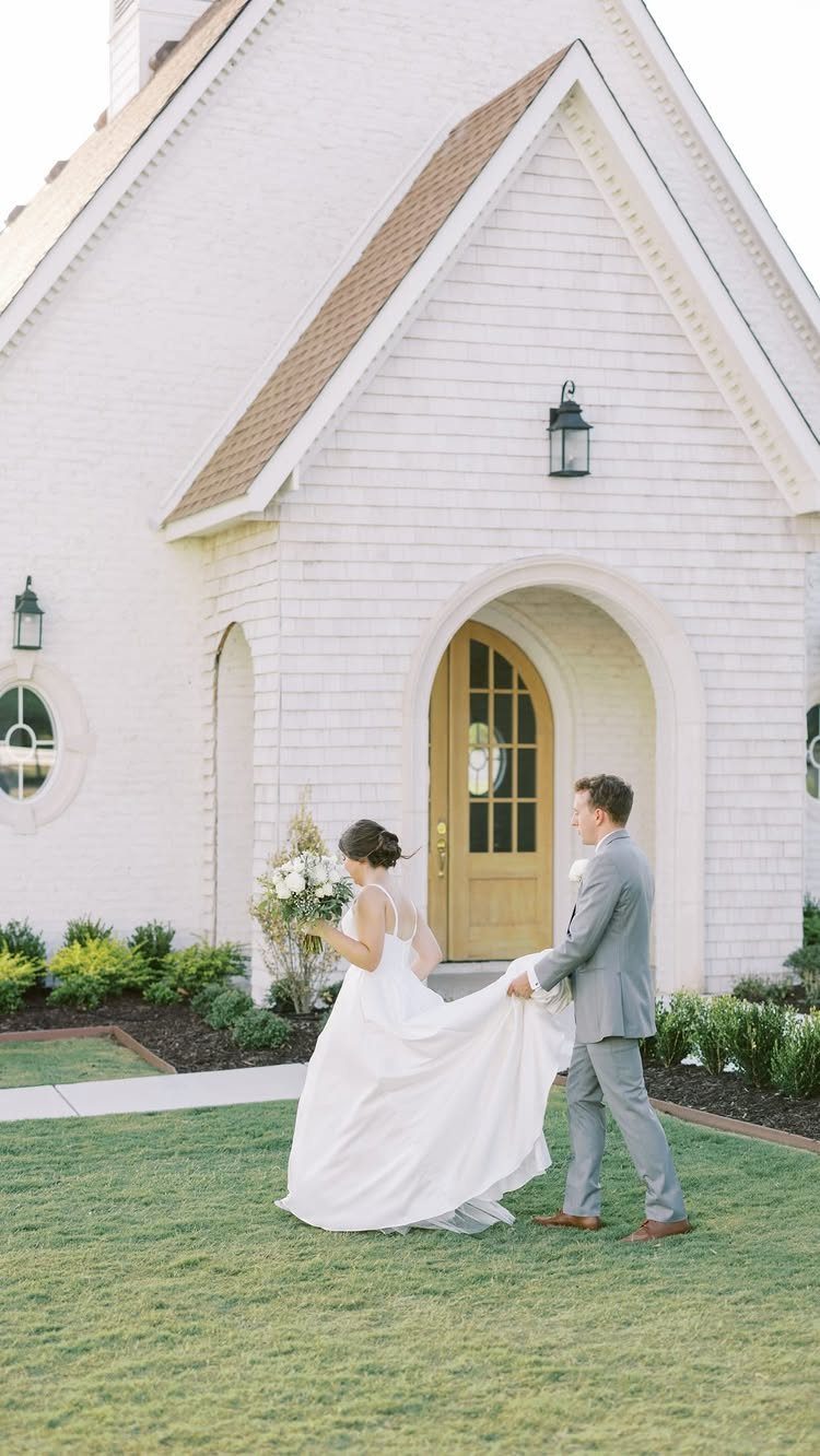 Bride and groom standing on a lawn before a white wooden wedding chapel.