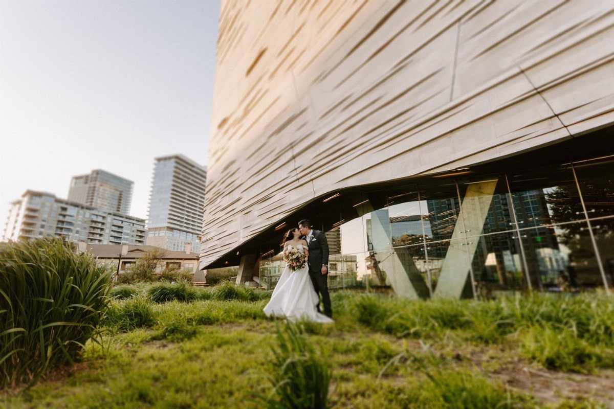 Bride and groom posing in front of the modern Perot Museum architectural building.