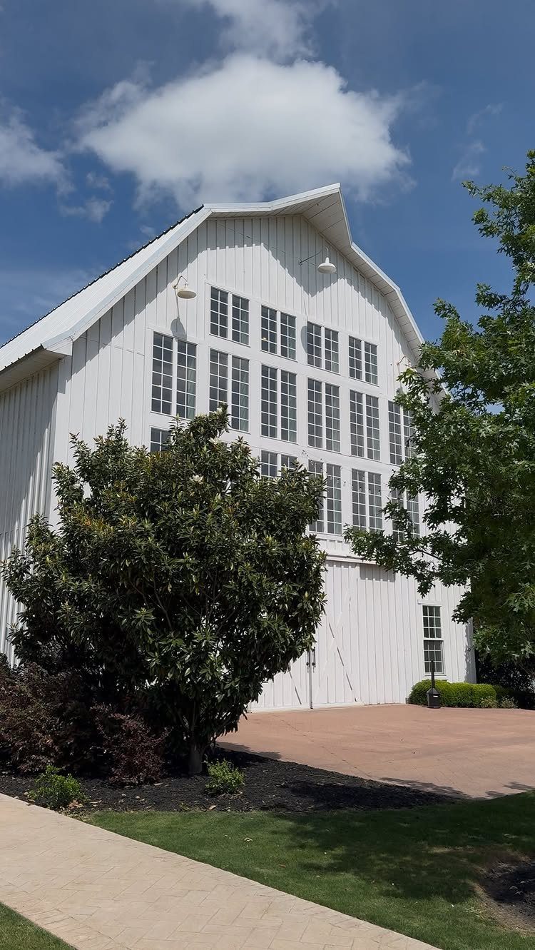 White barn venue with numerous windows surrounded by green trees and grass.