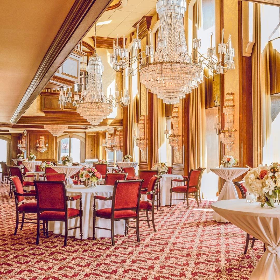 Elegant ballroom with crystal chandeliers, red patterned carpet, and set dining tables.