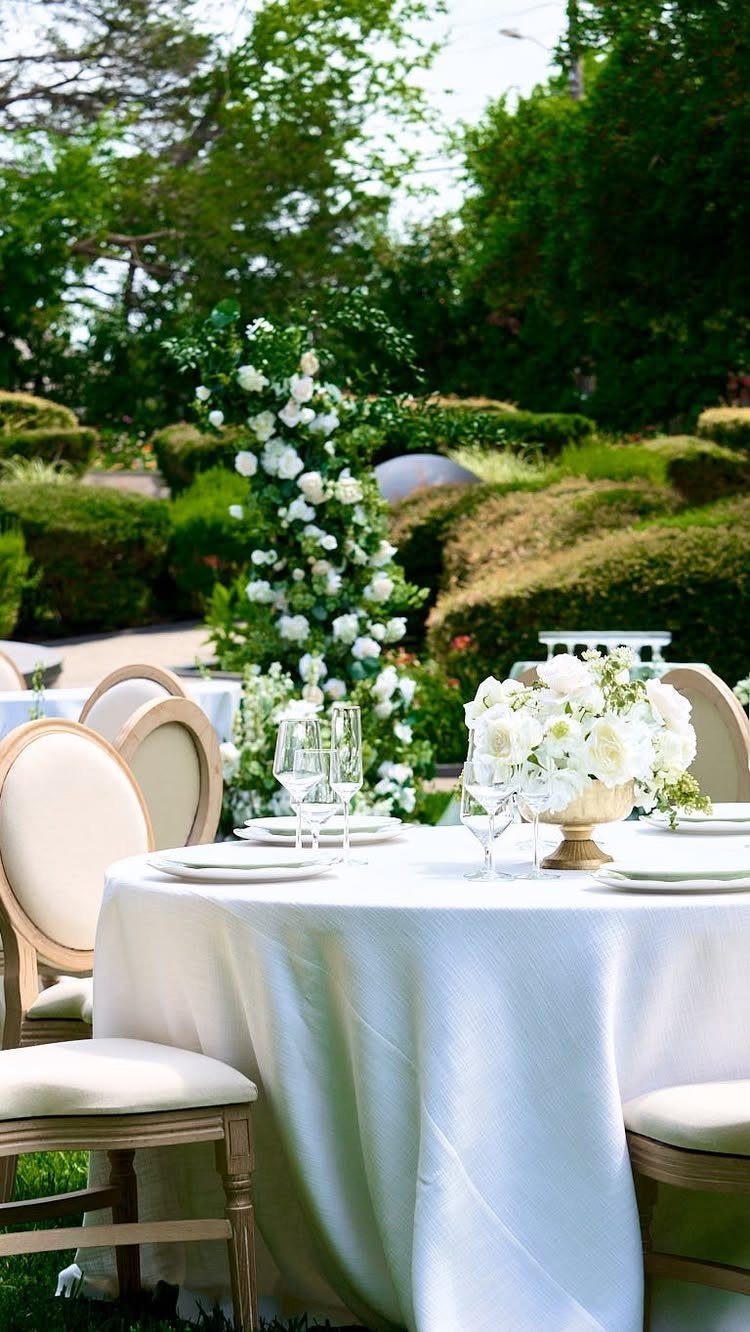 Round wedding table with white linens and floral centerpiece in a lush botanical garden.