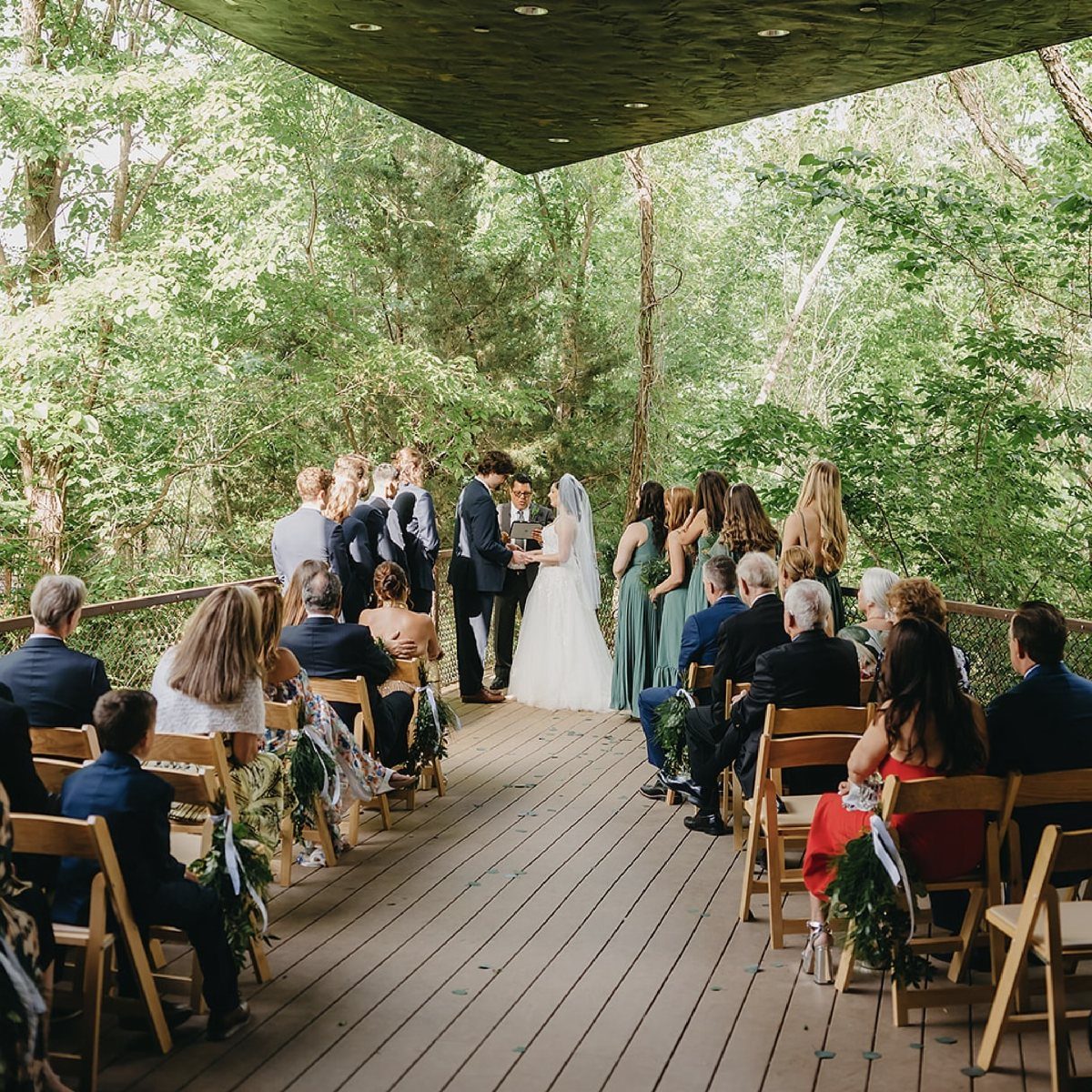 Wedding ceremony on a wooden deck surrounded by dense green forest trees.