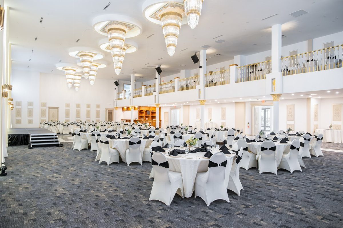 Hotel ballroom with round tables, white linens, black bows, and tiered crystal chandeliers.