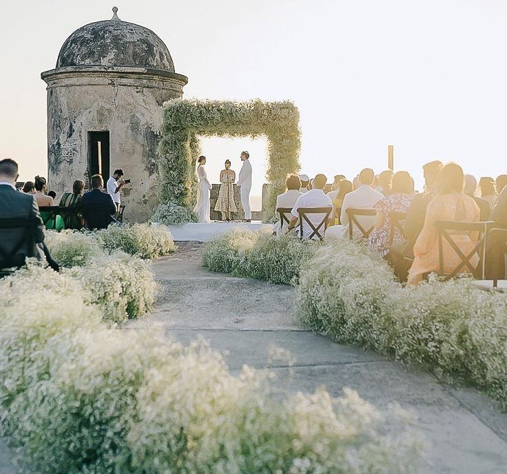 Wedding ceremony with a floral arch next to a historic stone turret building.