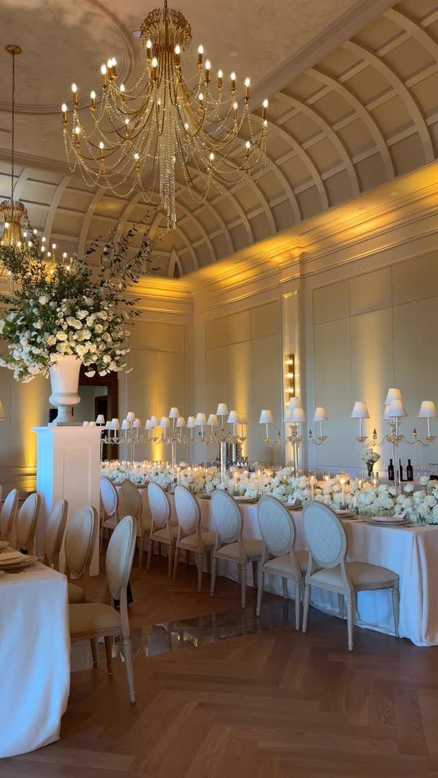 Luxury wedding banquet table with white flowers and candles under a crystal chandelier.