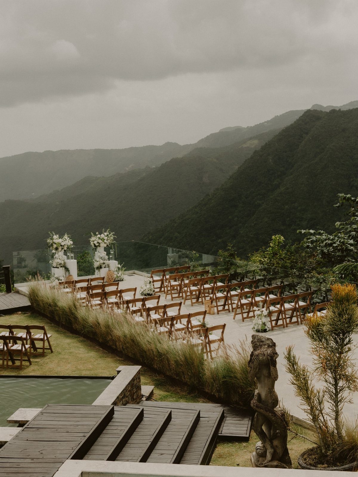Outdoor wedding ceremony setup with wooden chairs overlooking a lush green mountain landscape.