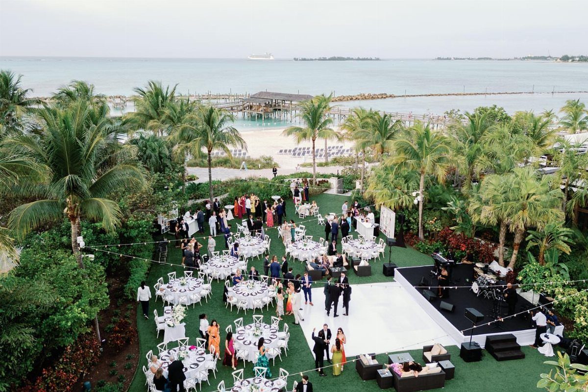 Outdoor wedding reception with white tables and palm trees overlooking a tropical beach.