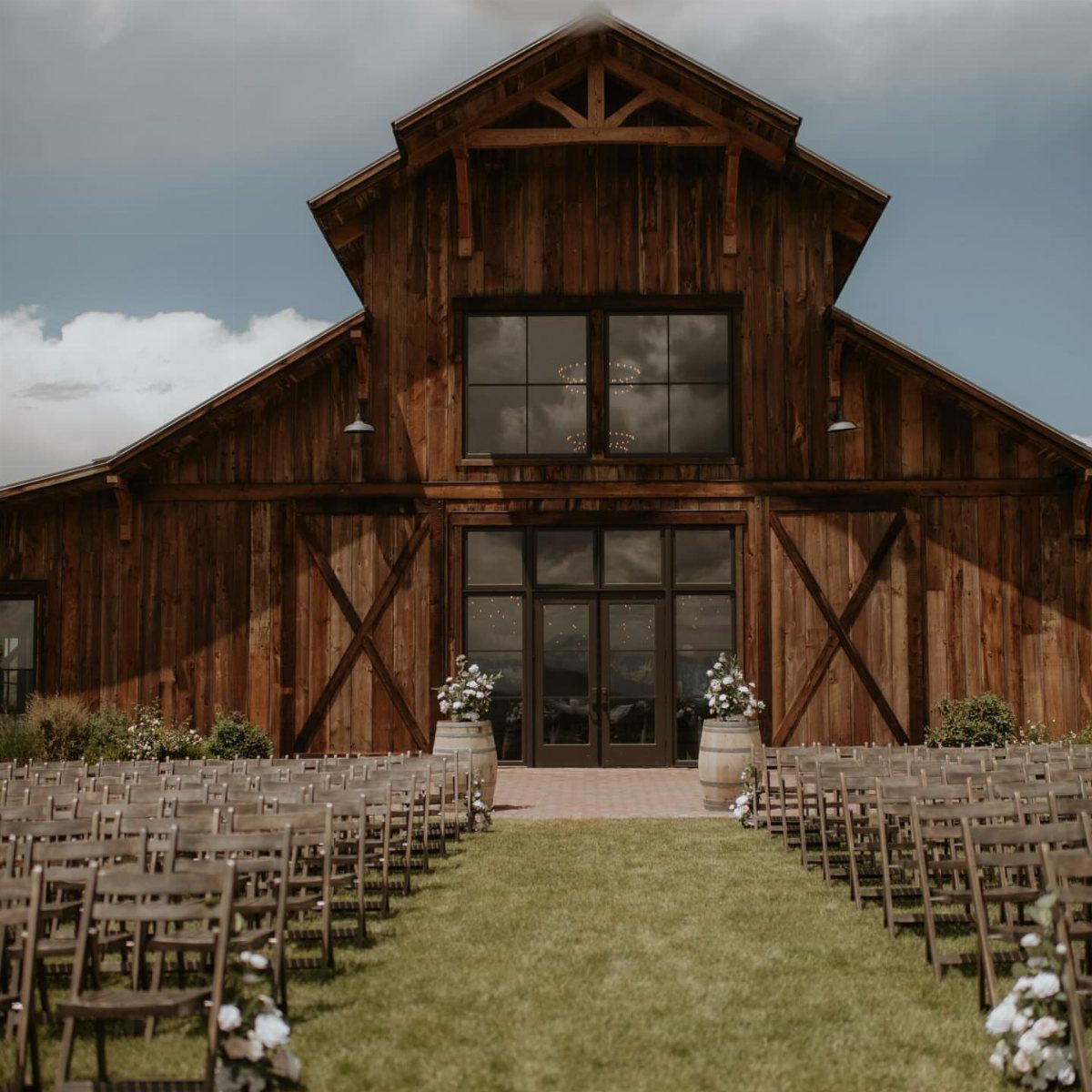 Wooden wedding chairs facing a large rustic barn for an outdoor ceremony venue.