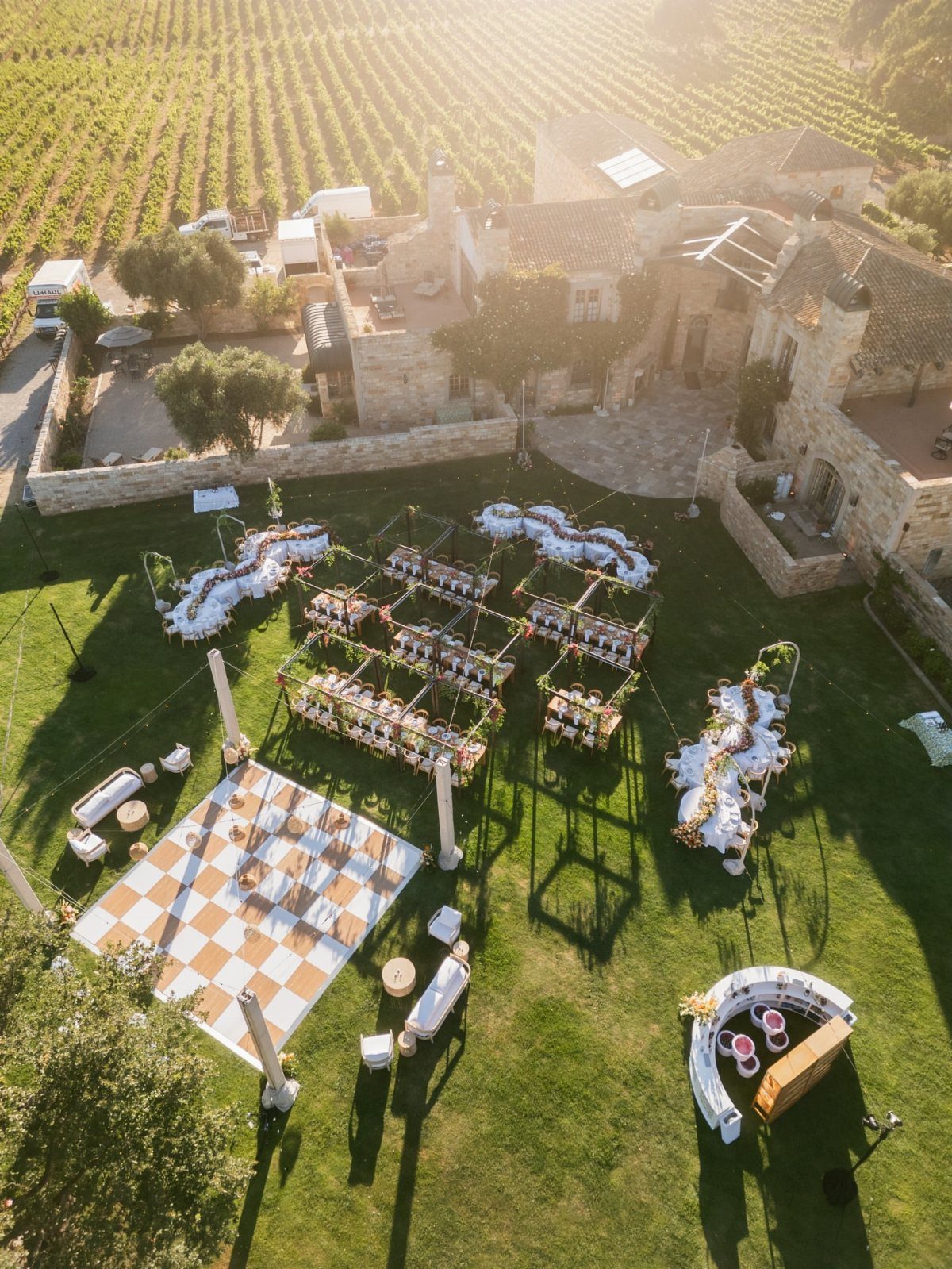 Outdoor wedding reception setup on a lawn with vineyards in the background.