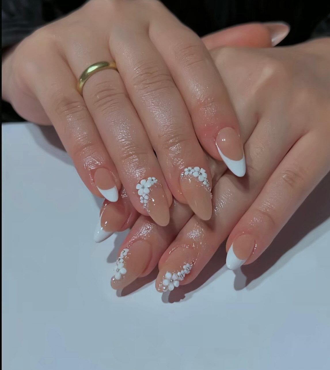 Almond-shaped nails with white French tips and 3D white floral nail art accents.