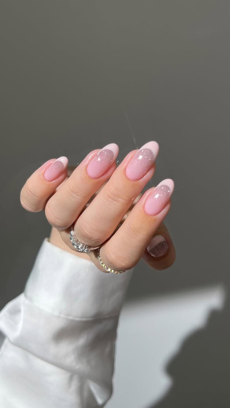 Almond-shaped nails with sheer pink polish and white glitter tips on a hand.