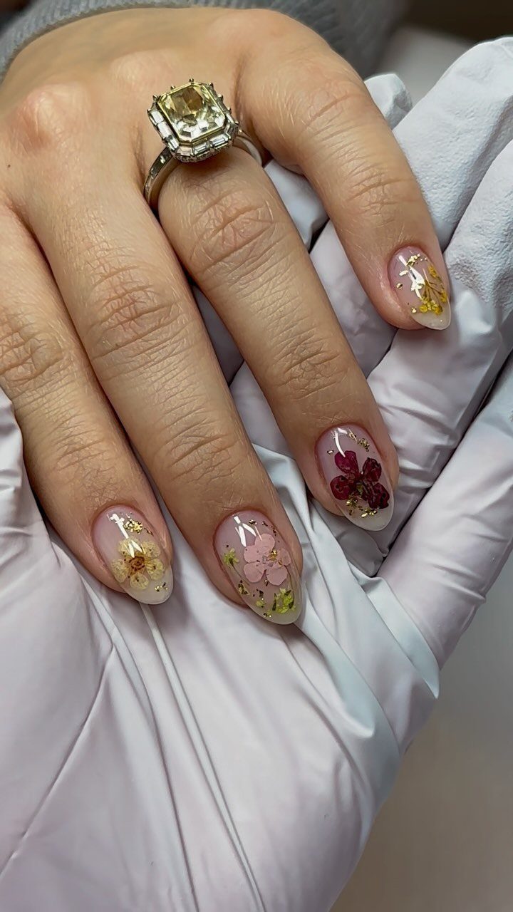 Almond nails with embedded dried flowers and a large diamond engagement ring