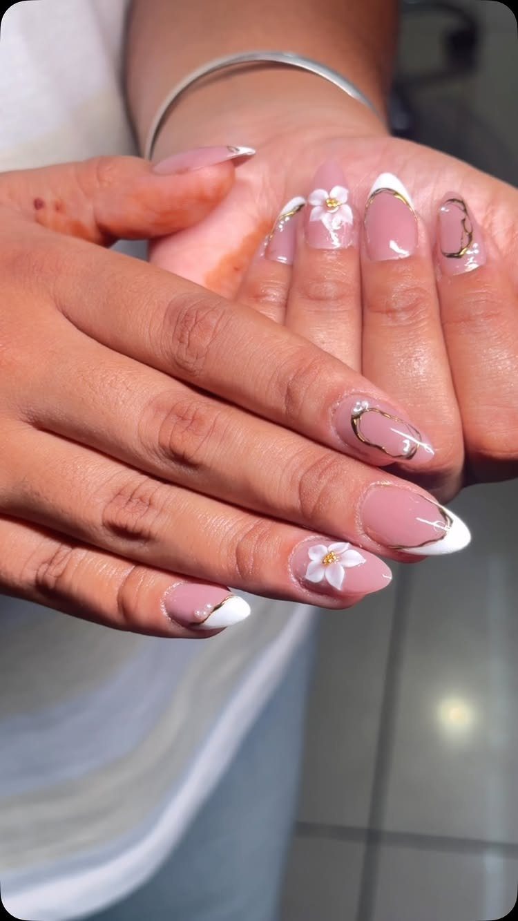 Almond-shaped nude and white French tip nails with small white 3D floral accents.