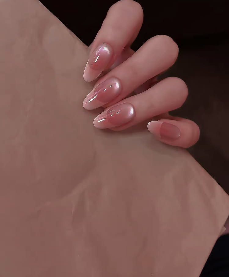 Almond shaped nails with a sheer pink pearlescent glazed finish on a hand.