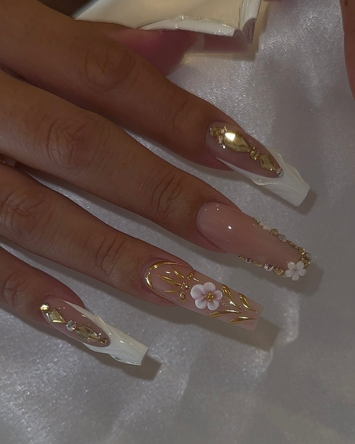 Almond-shaped wedding nails with nude polish, thin gold lines, and small white flowers.