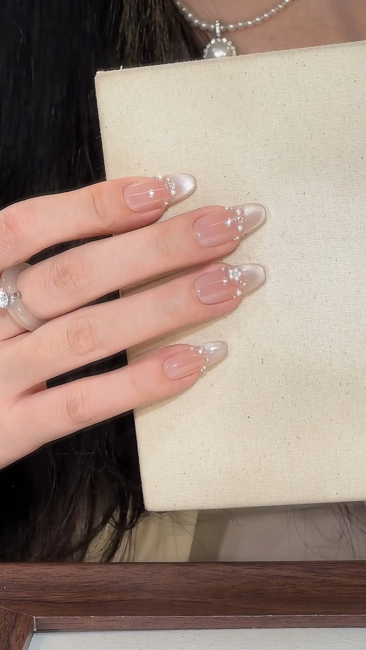 Hand with sheer pink nails and pearl accents holding a cream paper.