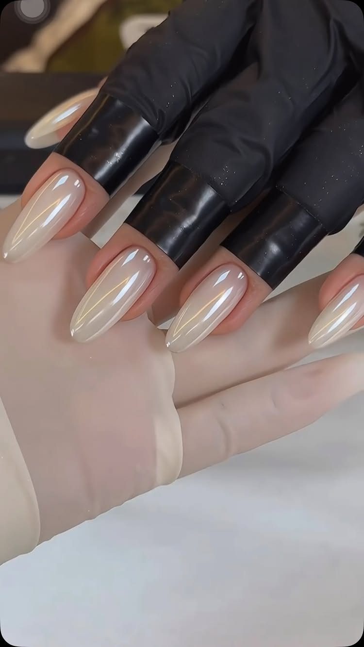 Pearlescent white almond-shaped nails held by hands in black and white gloves.