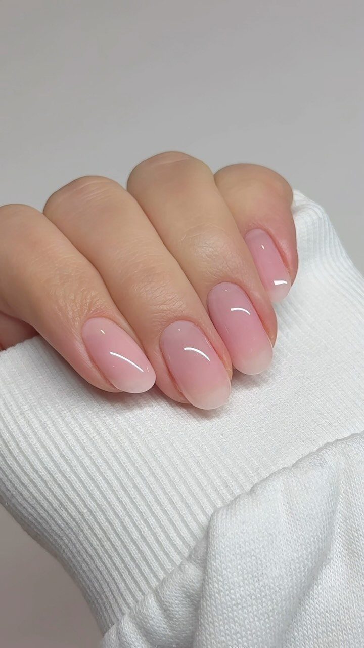 Almond-shaped nails with sheer pink glossy polish resting on a white ribbed sleeve.