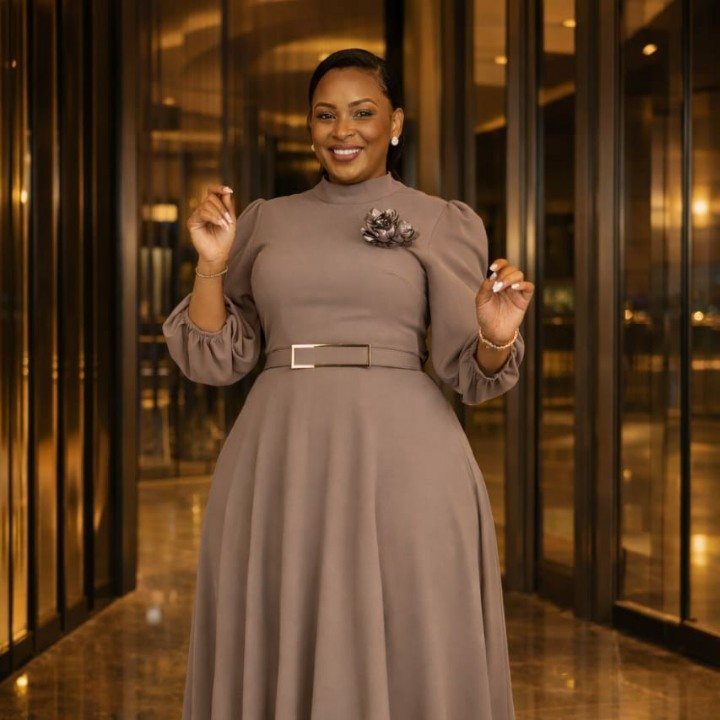 Woman in a taupe elegant long-sleeved dress with a floral brooch and belt.