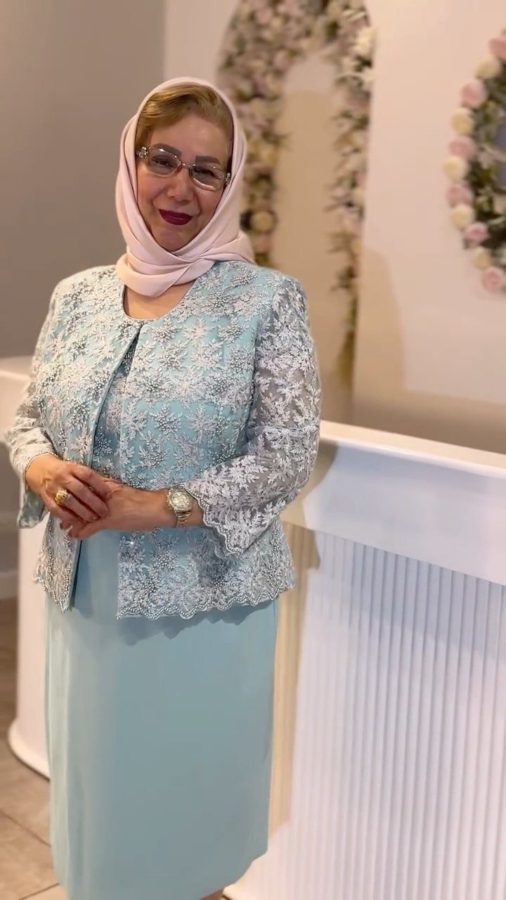 Woman over 50 wearing an elegant light blue lace dress and pink hijab.