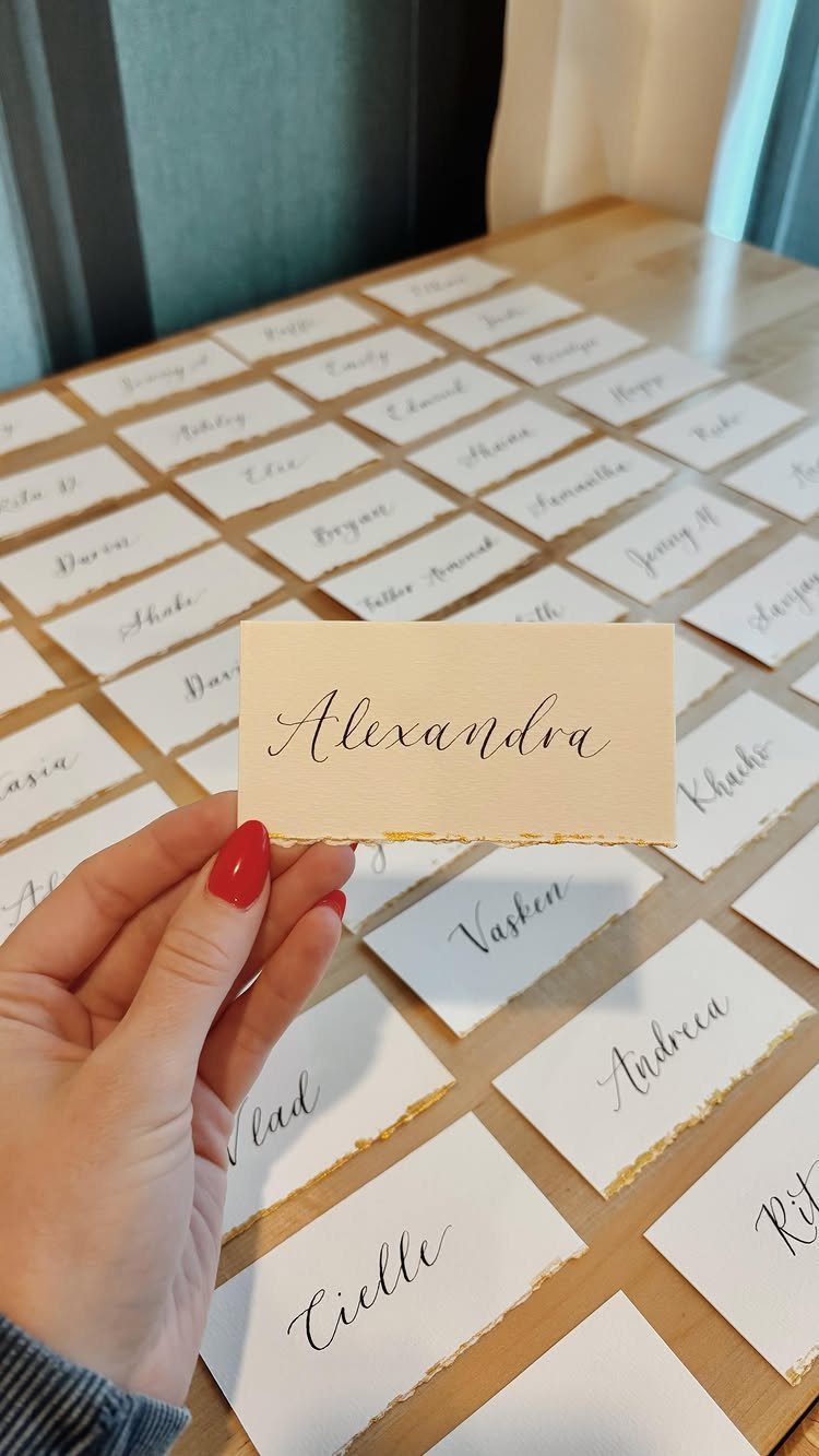 Hand holding a cream place card with elegant script calligraphy on a wooden table.