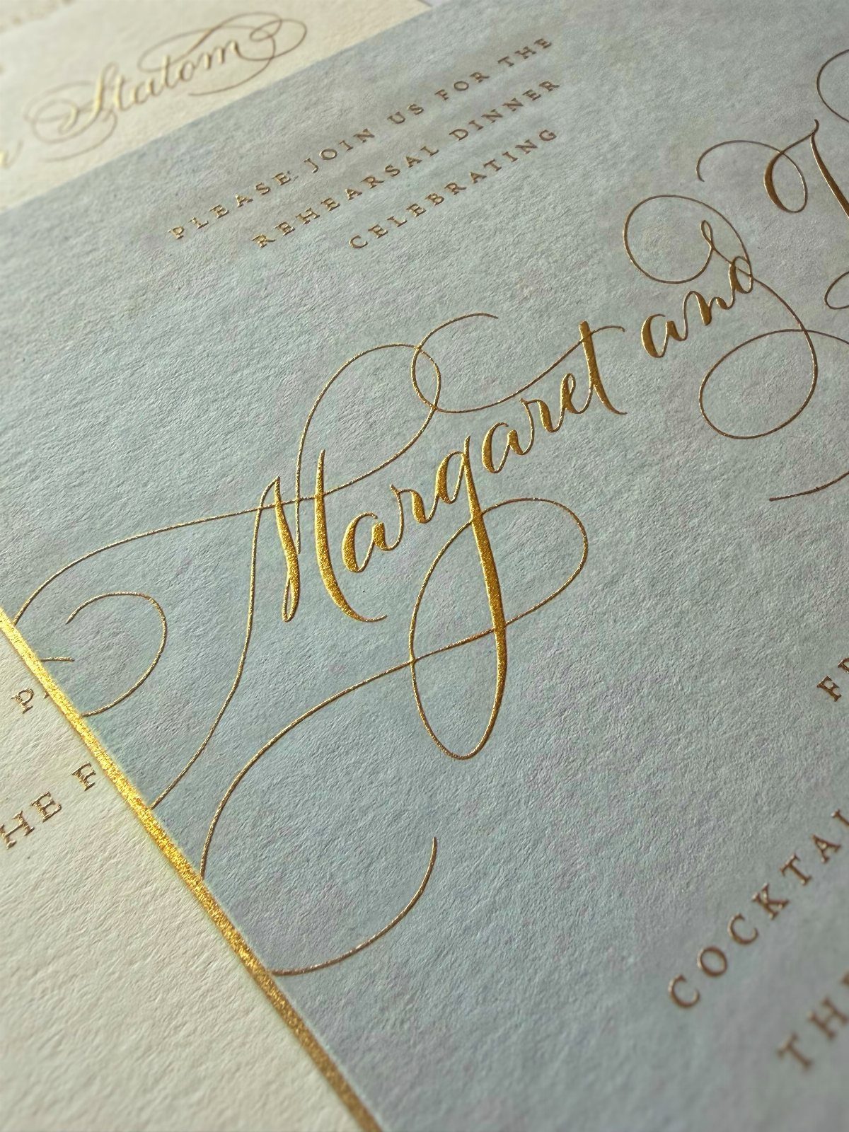 Gold foil calligraphy on light blue textured paper for a wedding invitation.
