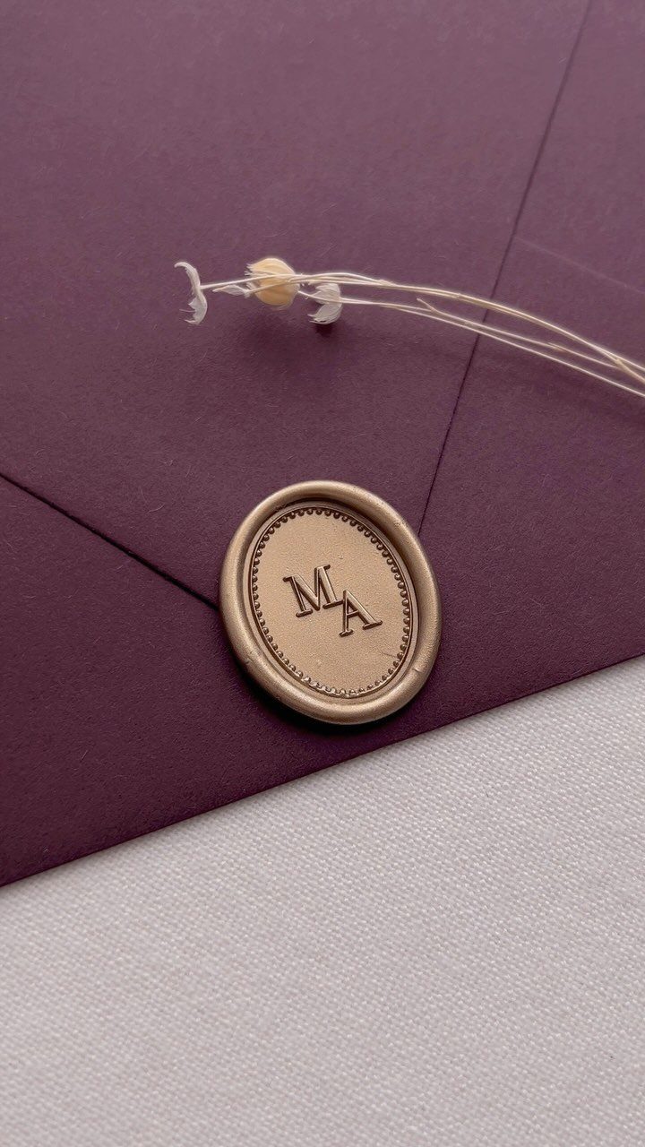 Gold wax seal with serif initials on a deep purple wedding envelope
