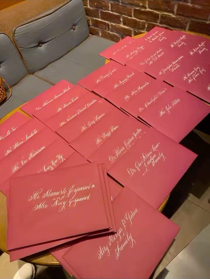 Pink envelopes with elegant white cursive calligraphy names arranged on a wooden table.