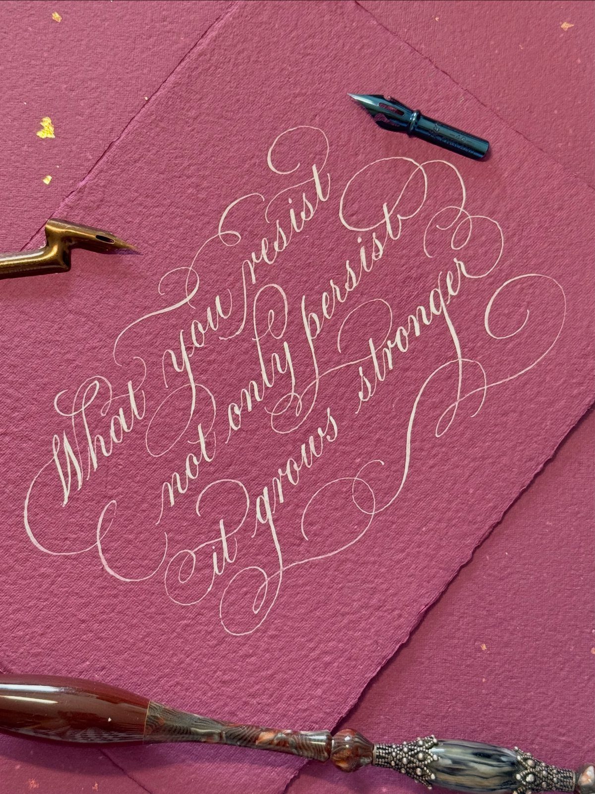 White calligraphy script on burgundy paper surrounded by three professional dip pens