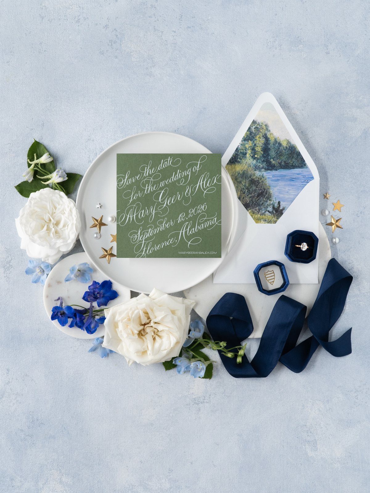 Green wedding invitation with white calligraphy surrounded by white and blue flowers.