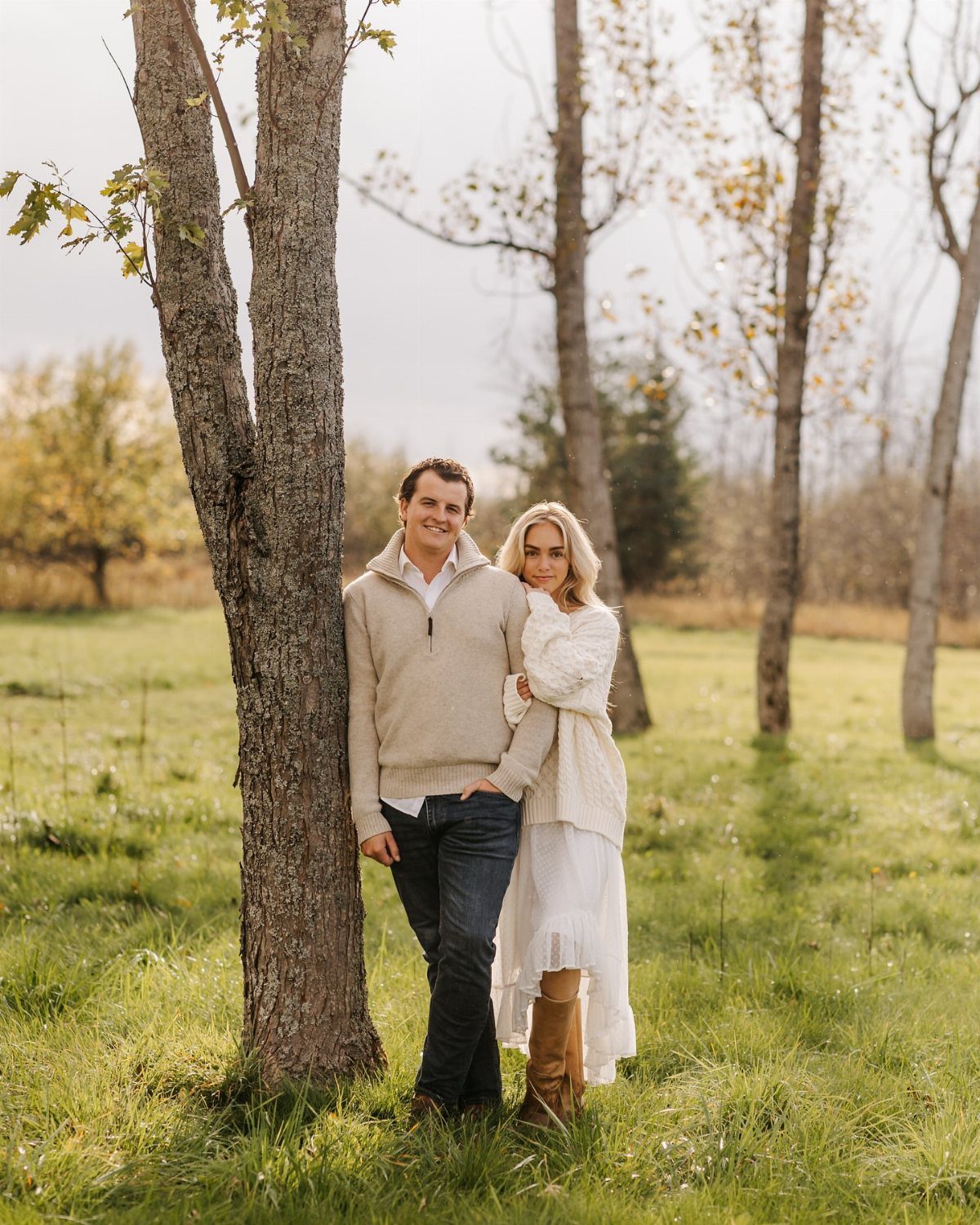 Couple posing in a field wearing beige and white autumn sweaters and boots.