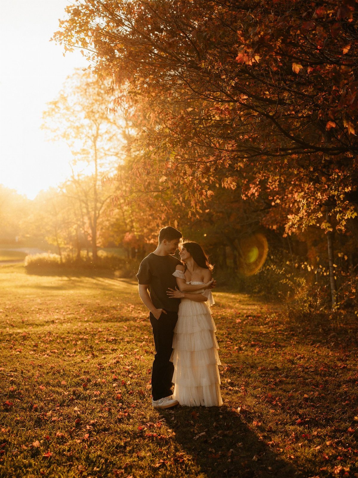 Couple embracing in a field under autumn trees during golden hour sunset