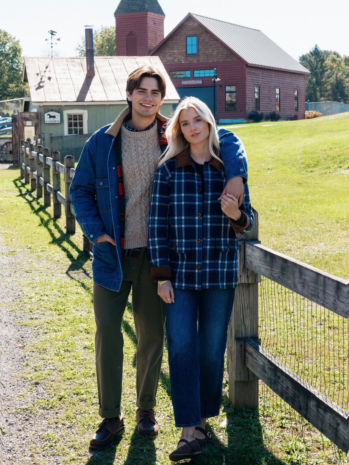 Couple posing in autumn clothing by a wooden fence with a red barn background.