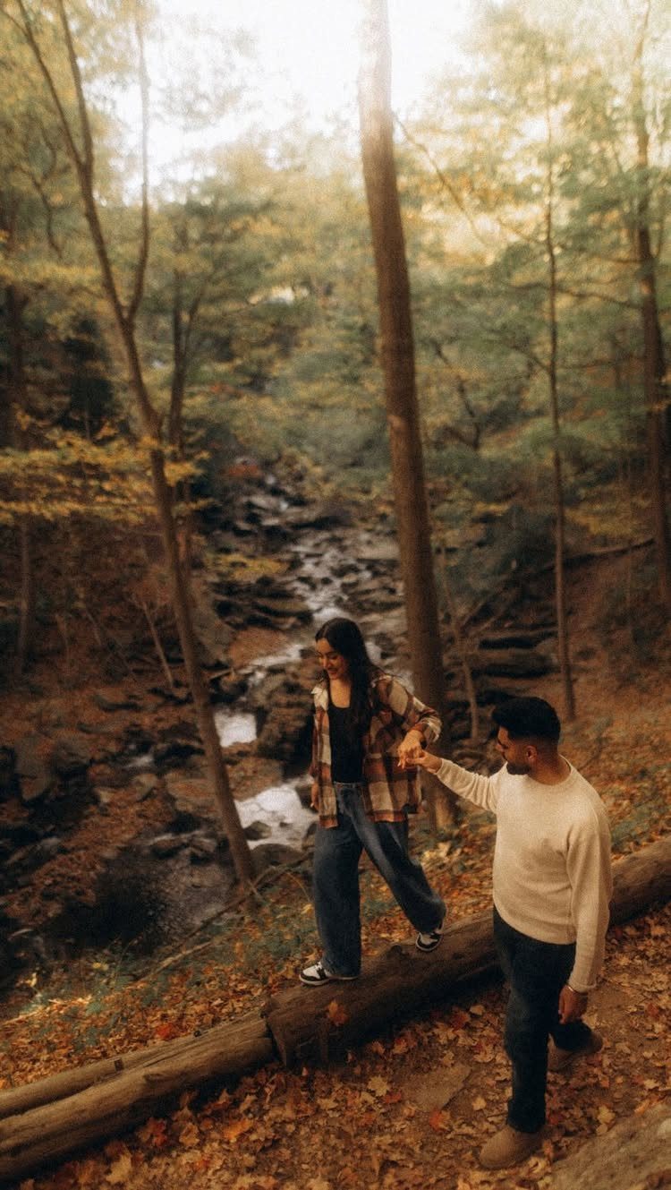 Couple in cream and plaid autumn clothing posing in a leaf-covered forest.