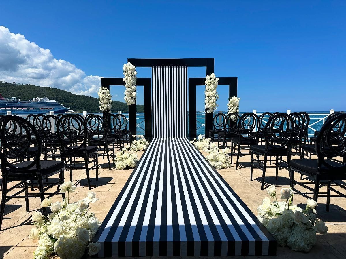 Black and white striped wedding aisle and backdrop with black chairs and white flowers.